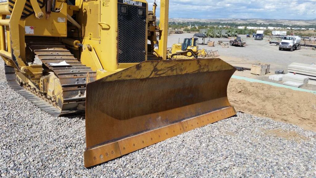 Close view of a Caterpillar pipelayer dozer blade and cutting edge, with the track behind it, in a New Mexico yard