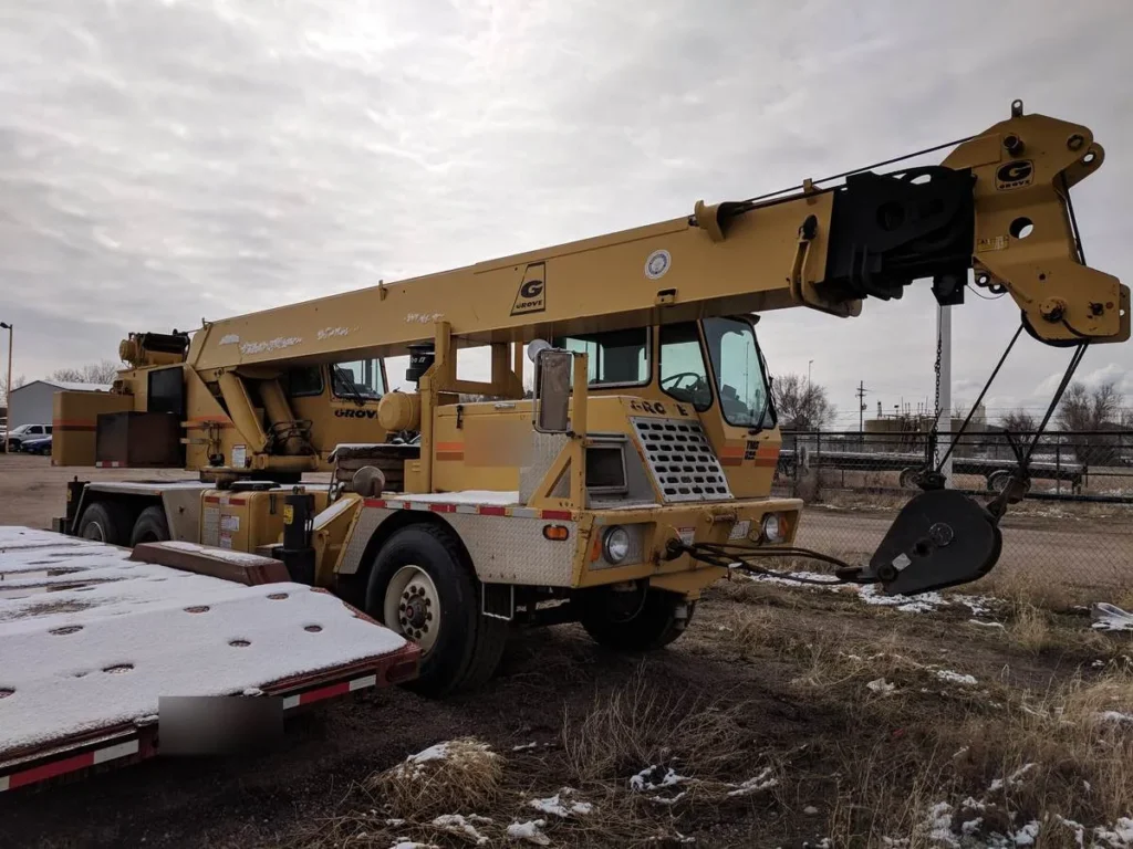 Grove TMS522 truck crane with its boom out and the hook block on the ground beside a lowboy trailer