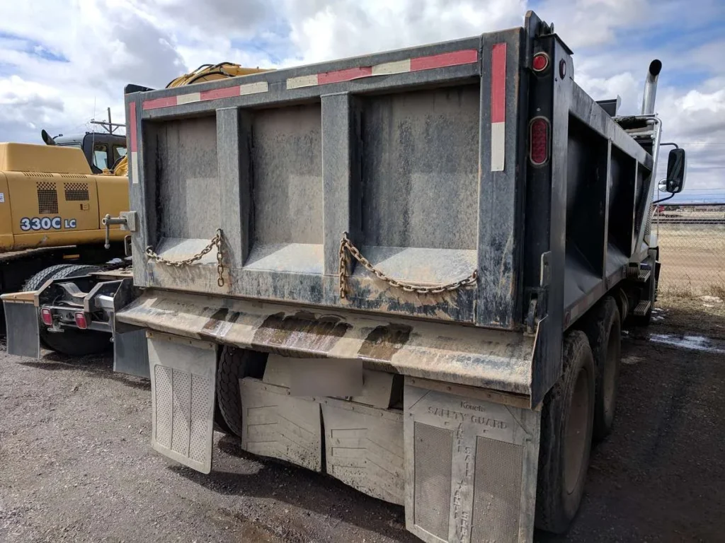 Rear of a dump truck body showing the tailgate, tailgate chains and the worn lip of the body floor